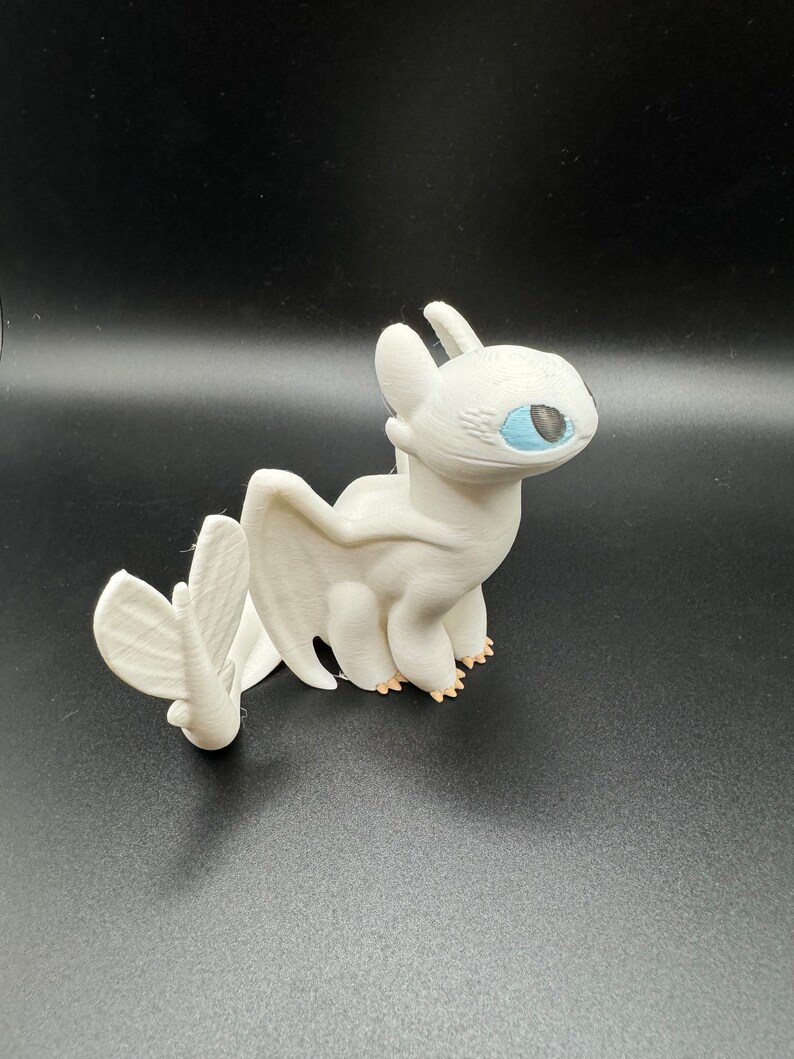 May include: White 3D printed figurine of a dragon with blue eyes and a curled tail. The dragon is standing on a black surface.