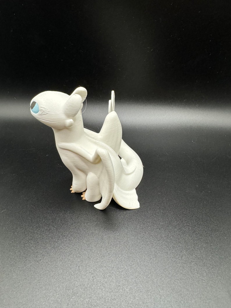 May include: White figurine of a dragon with a blue eye. The dragon has wings and a tail. The figurine is made of plastic.