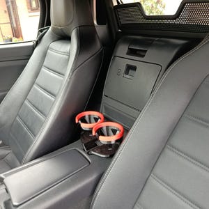 May include: Interior view of a car with black leather seats and red cup holders. The seats have white stitching and a quilted pattern. The car's interior is dark, with a focus on the seats and cup holders.