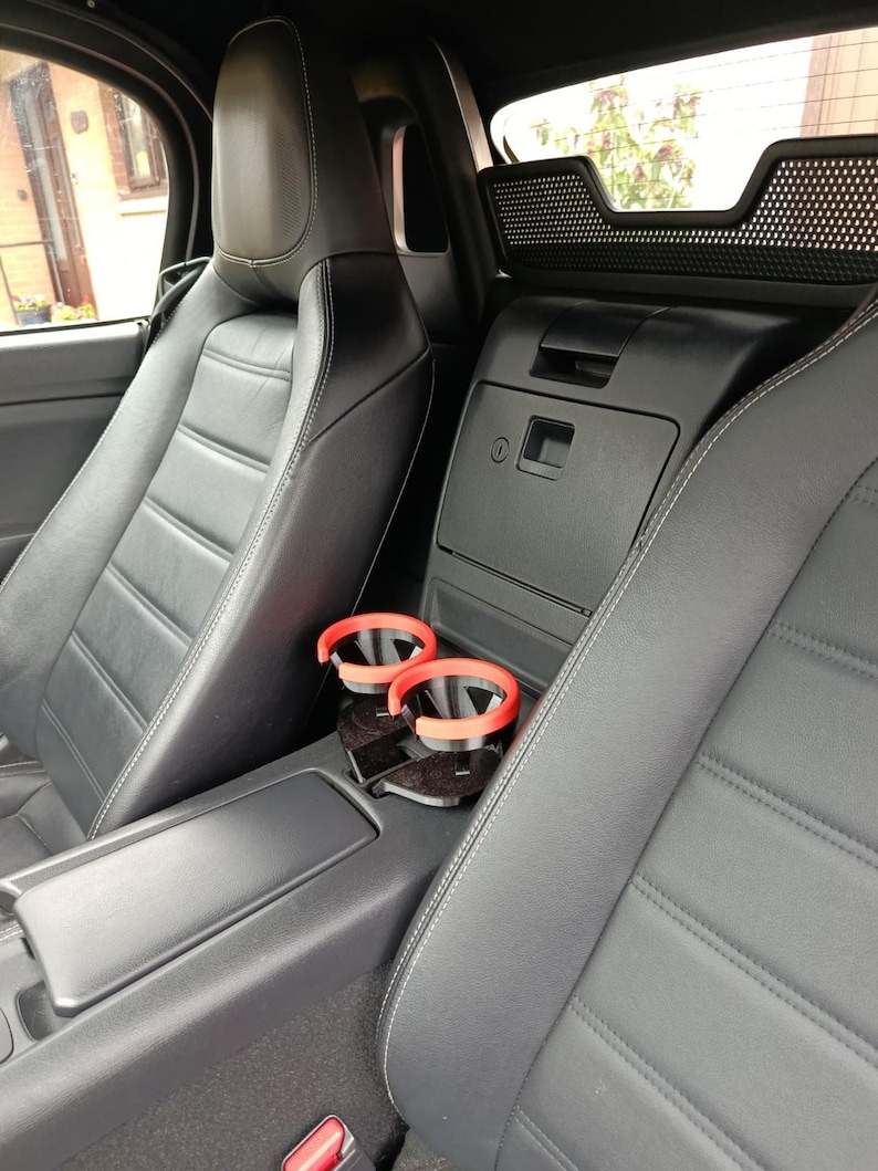 May include: Interior view of a car with black leather seats and red cup holders. The seats have white stitching and a quilted pattern. The car's interior is dark, with a focus on the seats and cup holders.