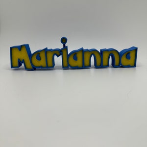 May include: A 3D printed name sign with the name "Marianna" in yellow letters with a blue outline.