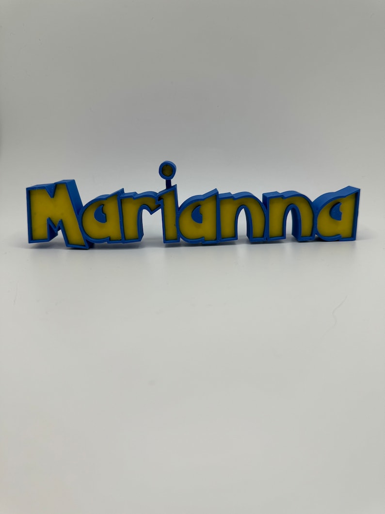May include: A 3D printed name sign with the name "Marianna" in yellow letters with a blue outline.