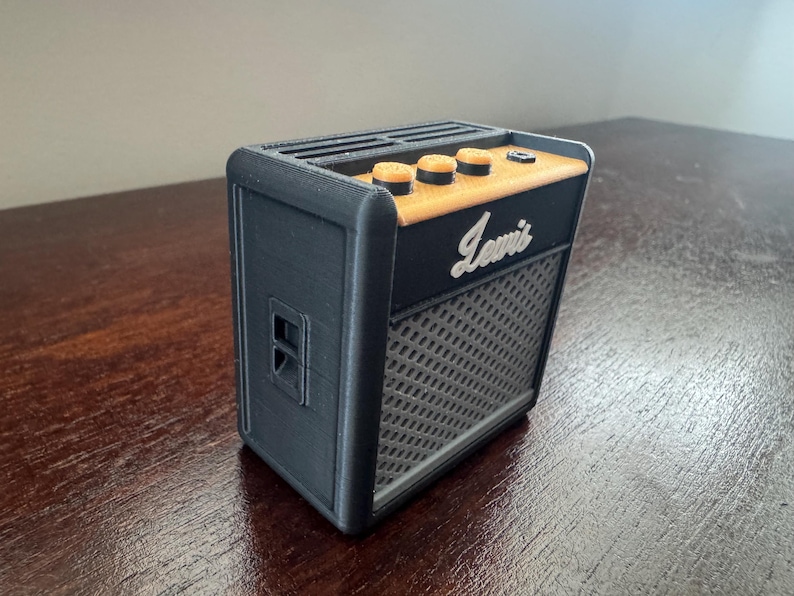 May include: A black and orange electric guitar amplifier with the word "Lewitt" printed on the front.