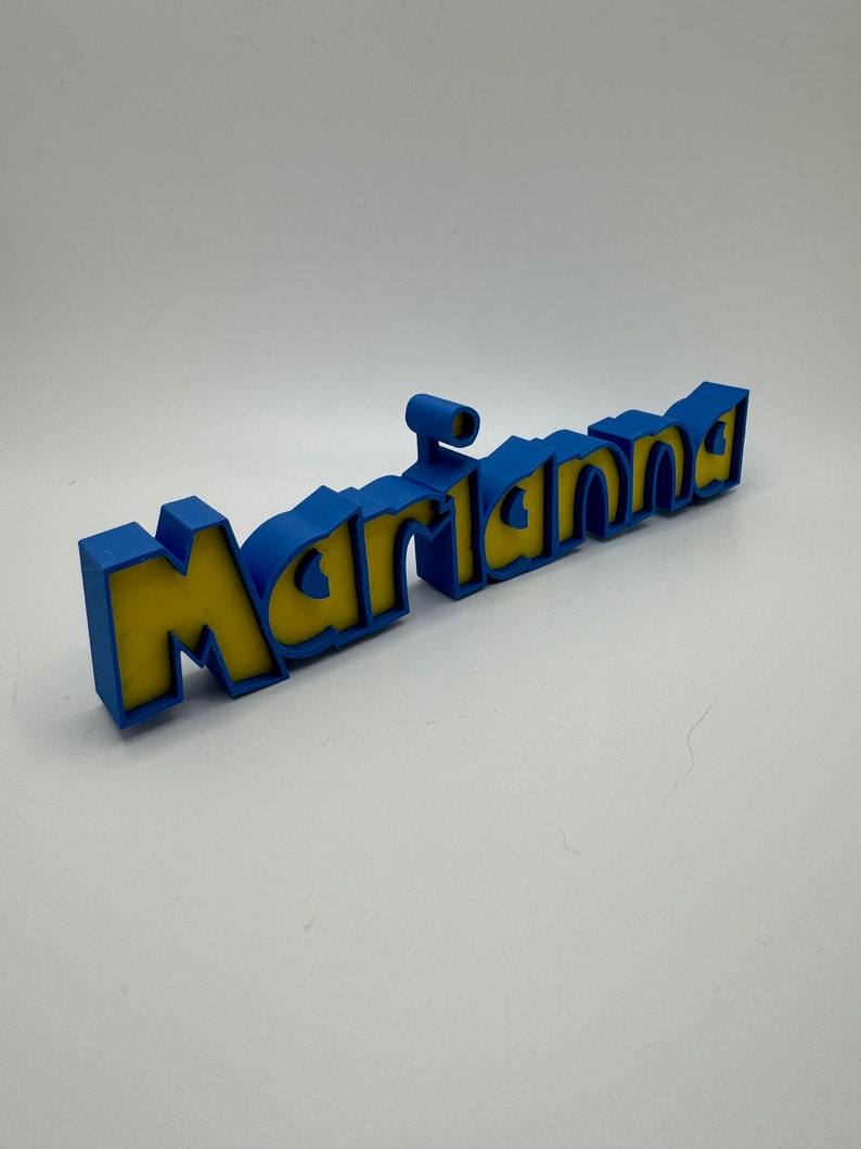 May include: A 3D printed name sign that says "Marianna" in blue letters with yellow fill. The letters are raised and have a rounded, playful font.