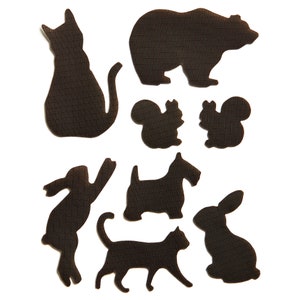 May include: A collection of black animal silhouettes, including a cat, bear, squirrels, rabbit, dog, and a second cat. The shapes are cut from a textured material and arranged against a white background.