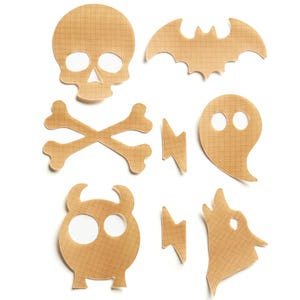 May include: A collection of tan adhesive patches featuring a grid pattern. The set includes a skull, a bat, crossbones, two lightning bolts, a ghost, a horned creature, and a howling wolf shape, all with die-cut openings for eyes or features.