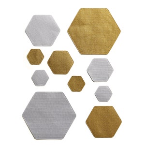 Puede incluir: Un juego de nueve manteles individuales hexagonales en dos colores: dorado y plateado. Los manteles individuales están hechos de una tela texturizada y están dispuestos en un patrón de panal.
