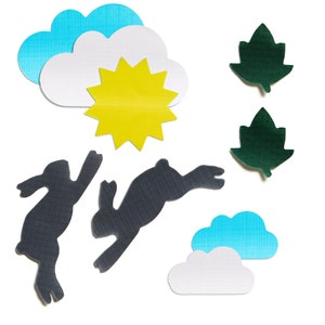 May include: Paper cutouts of two black rabbits jumping, a yellow sun, two blue clouds, and two green leaves.