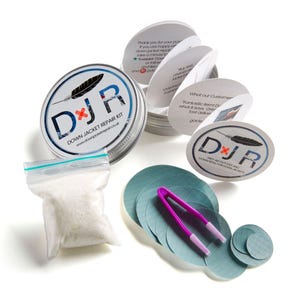 Könnte beinhalten: Eine silberne Dose mit einem weißen Deckel, die ein Reparaturset für Daunenjacken enthält. Das Set beinhaltet einen kleinen Beutel mit Daunen, eine Pinzette und einen Satz runder Flicken in verschiedenen Größen. Die Dose trägt ein Etikett mit der Aufschrift "DJR Down Jacket Repair Kit" und einer Website-Adresse. Der Deckel der Dose trägt ein Etikett mit der Aufschrift "First Aid Patches and Downproof for Down Jackets".