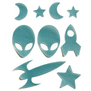 Op de afbeelding: Een set blauwe papieren uitsnijdingen van ruimtethema's, waaronder sterren, manen, aliens en raketten. De uitsnijdingen zijn op een witte achtergrond.