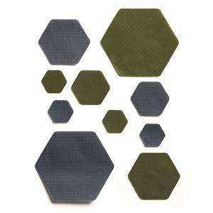 Può includere: Una collezione di toppe in tessuto esagonali in tonalità di verde e grigio. Le toppe sono disposte in un motivo casuale.