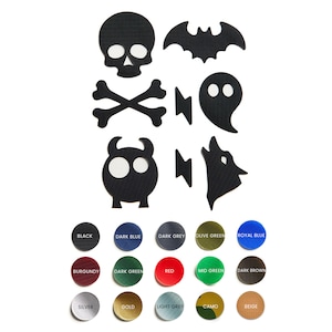 May include: A set of 10 black iron-on patches featuring Halloween-themed designs, including a skull, crossbones, bat, ghost, monster, wolf, and lightning bolts. The patches are shown against a white background with a color chart of 15 different colors.