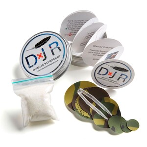 Könnte beinhalten: Eine silberne Dose mit einem weißen Etikett, auf dem "DJR Down Jacket Repair Kit" und eine Website-Adresse stehen. Die Dose ist geöffnet und enthält einen kleinen Beutel mit weißen Daunen und einen Satz Tarnstoff-Flicken. Die Flicken sind in einem Kreis um eine Pinzette angeordnet.