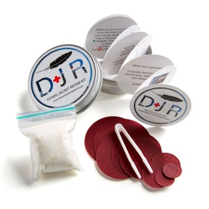 May include: A silver tin with a red and white logo that says "D+JR Down Jacket Repair Kit" and a website address. The tin is open and contains a small bag of white down feathers, a set of red fabric patches, and a pair of tweezers.