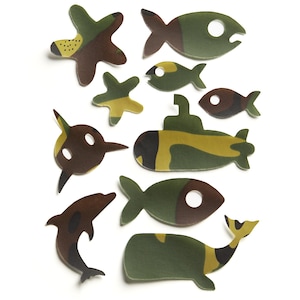 Può includere: Una collezione di forme piatte fustellate con un motivo mimetico nei toni del verde oliva, marrone e marrone chiaro. Il set include vari animali marini come pesci, un delfino e una balena, insieme a un sottomarino e una forma di stella marina.