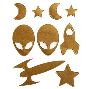 May include: A set of gold-colored felt cutouts featuring a rocket, stars, moons, and alien heads. The cutouts are perfect for crafting projects, scrapbooking, or decorating.