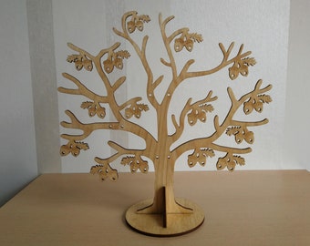 Puede incluir: Un organizador de joyas en forma de árbol de madera, con una base redonda y ramas adornadas con recortes de bellotas y hojas. El color natural de la madera y el diseño detallado crean una exhibición decorativa para aretes y collares.