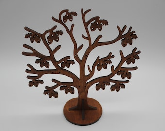 Puede incluir: Un expositor en forma de árbol de madera marrón oscuro, con base redonda y ramas adornadas con recortes en forma de bellotas. Diseñado para exhibir joyas u objetos pequeños. El árbol mide aproximadamente 20 cm de altura.