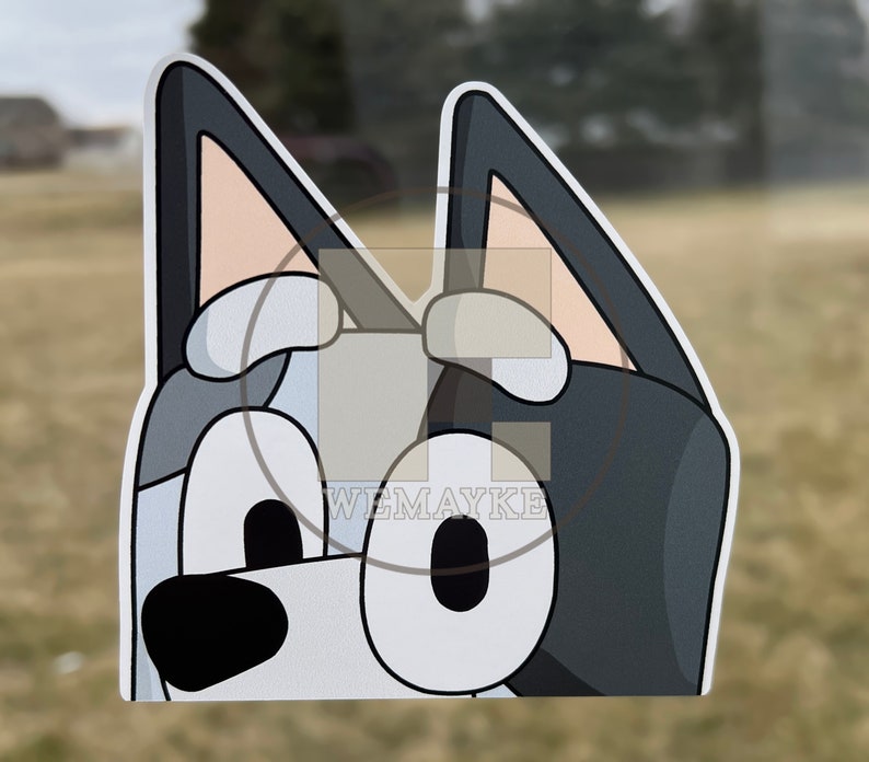May include: A die-cut vinyl sticker featuring a cartoon dog character with large oval eyes, a black nose, and pointed ears. The character has a color palette of dark gray, light gray, and white. The text WEMAYKE is printed in white on the sticker.