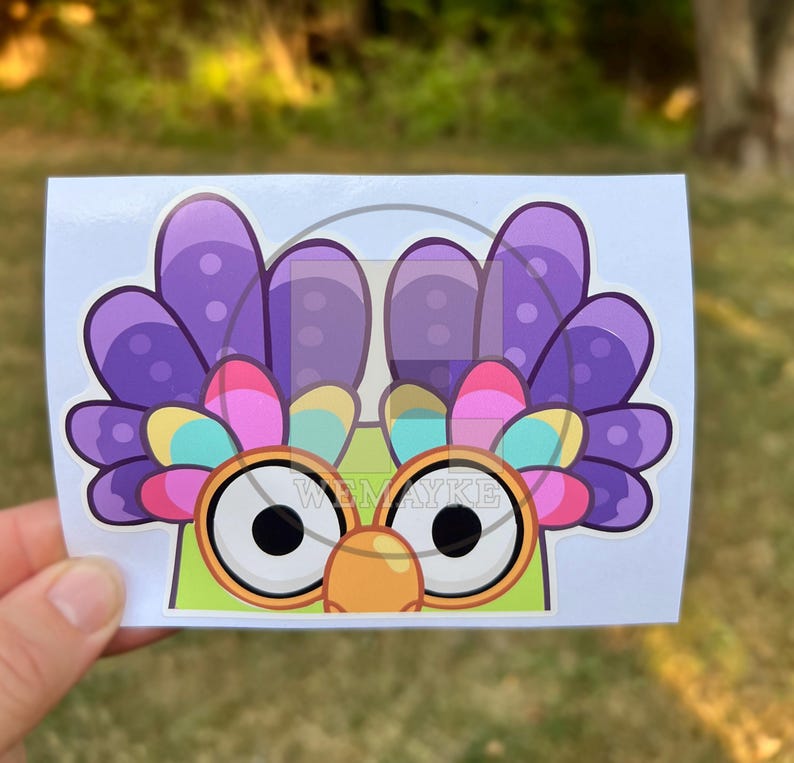 May include: A rectangular sticker featuring a cartoon character with large white eyes, orange circular glasses, and a green face. The character has a vibrant crest of purple, pink, yellow, and blue feathers. The text WEMAYKE is printed in the center.