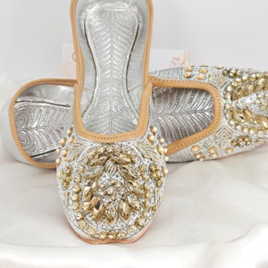 Peut inclure: Une paire de chaussures plates argent&eacute;es orn&eacute;es de strass dor&eacute;s et blancs. Les chaussures ont une pointe pointue et un talon bas.
