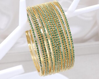 May include: A set of ten gold bangles with green gemstones. The bangles are stacked on top of each other and are arranged in a circular pattern.