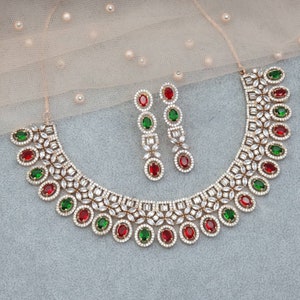 Peut inclure: Un collier et des boucles d'oreilles en or avec un motif de pierres blanches, rouges et vertes. Le collier a une cha&icirc;ne d&eacute;licate avec un pendentif orn&eacute; d'un groupe de pierres. Les boucles d'oreilles sont des boucles d'oreilles pendantes avec un motif de pierres similaire.