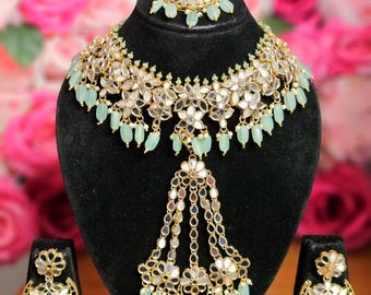 May include: A gold and silver necklace set with a large, ornate pendant and matching earrings. The necklace features a floral design with mirror accents and light green beads. The earrings are also floral with mirror accents and light green beads.