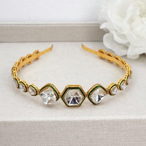 May include: A gold headband with a row of clear, faceted gemstones set in green enamel. The headband is flexible and has a delicate design.