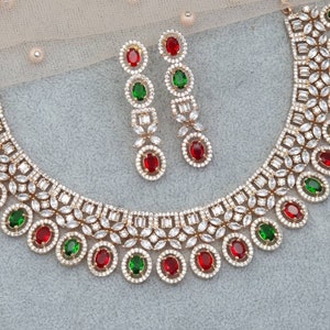 Peut inclure: Un collier et des boucles d'oreilles en or sertis de pierres de zircone cubique blanches et de pierres pr&eacute;cieuses rouges et vertes. Le collier a un motif floral et les boucles d'oreilles sont de style pendantes.