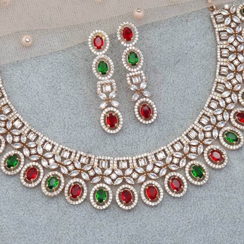 Peut inclure: Un collier et des boucles d'oreilles en or sertis de pierres de zircone cubique blanches et de pierres pr&eacute;cieuses rouges et vertes. Le collier a un motif floral et les boucles d'oreilles sont de style pendantes.