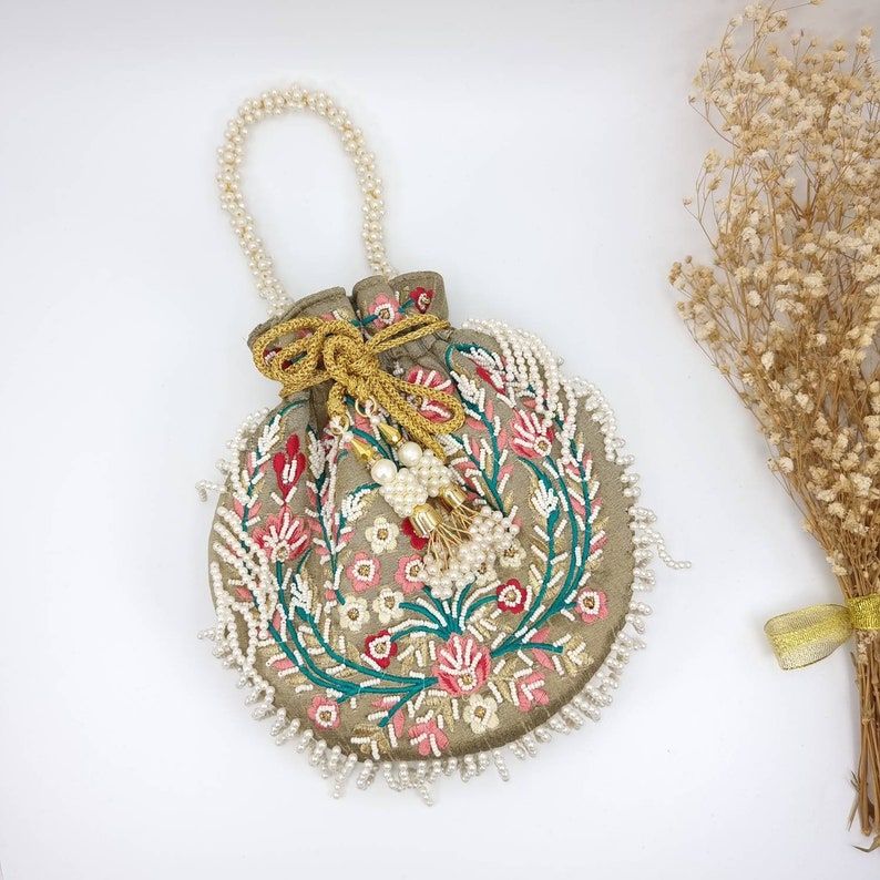 May include: A gray fabric drawstring bag with a floral embroidery design. The bag is decorated with white pearl beads and a gold tassel.