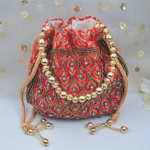 Puede incluir: Una bolsa de cord&oacute;n roja con bordados dorados y ribetes de cuentas. La bolsa tiene un borla dorada y un asa de cadena dorada.