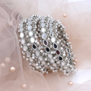 May include: A set of silver anklets with multiple rows of teardrop-shaped mirror charms and white pearl beads.
