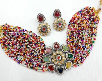 May include: A multi-strand beaded necklace with a colorful mix of beads. The necklace has a large, ornate pendant with a floral design and colorful gemstones. Matching earrings with a similar design are also included.