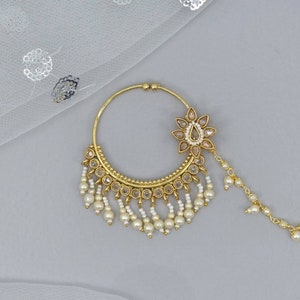 May include: A gold nose ring with a pearl and rhinestone design. The ring has a dangling chain with pearls and a floral design.