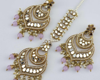 May include: A set of gold-tone earrings and a matching maang tikka, featuring mirrored and pearl accents. The earrings and tikka have dangling pink beads.
