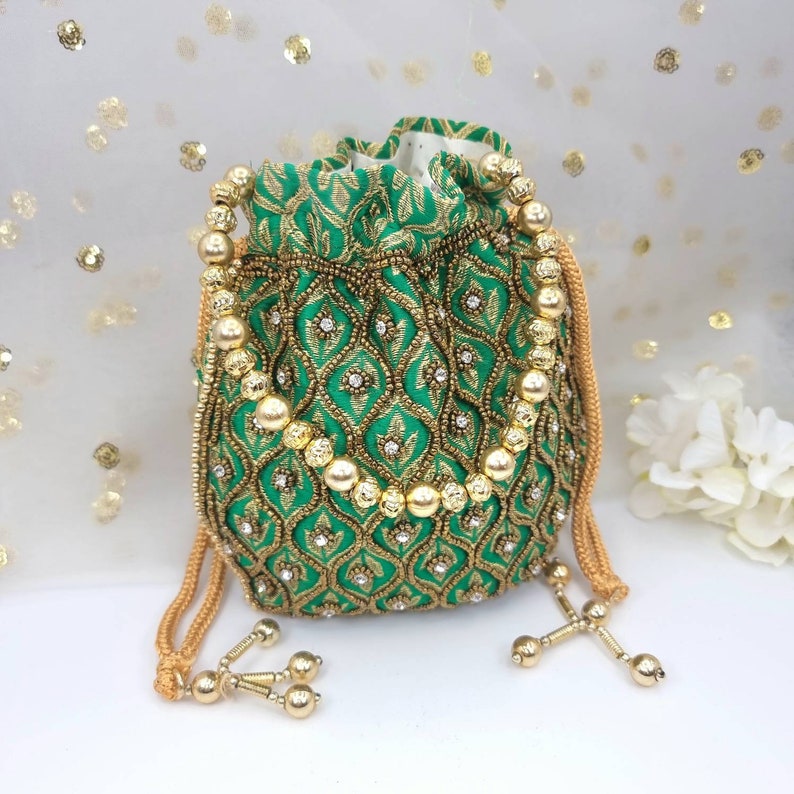 Puede incluir: Una bolsa de cord&oacute;n verde con bordados dorados y ribetes de cuentas. La bolsa tiene una correa de cadena dorada y detalles de borlas.