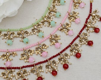May include: Three beaded necklaces in light green, light pink, and deep red. Each necklace features a strand of small faceted beads with dangling gold-tone metal charms, each set with a clear stone, small white faux pearls, and a larger round bead.