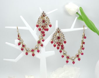 May include: A pair of gold-tone earrings with pink and white stones. The earrings are hanging from a white stand.