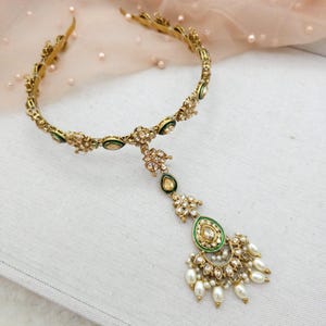 May include: Gold-toned headpiece with floral and teardrop designs. The headpiece features green enamel accents and is adorned with clear crystals and faux pearls. The design includes a central pendant with a teardrop shape and dangling pearls.