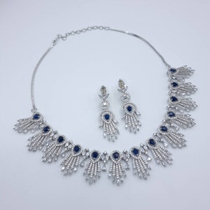 May include: A silver-toned jewelry set featuring a necklace and matching earrings. The necklace and earrings have a repeating design of clear and dark blue stones. The necklace is approximately 16 inches long.