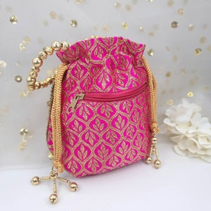 Puede incluir: Una bolsa de cord&oacute;n rosa con una cremallera dorada y un ribete de cuentas doradas. La bolsa tiene un patr&oacute;n floral y es perfecta para llevar objetos peque&ntilde;os.