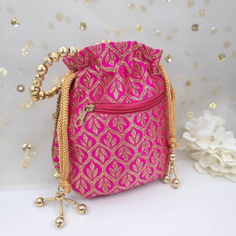 Puede incluir: Una bolsa de cord&oacute;n rosa con una cremallera dorada y un ribete de cuentas doradas. La bolsa tiene un patr&oacute;n floral y es perfecta para llevar objetos peque&ntilde;os.