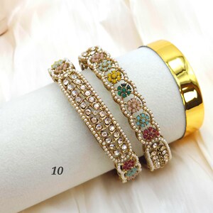 May include: Two gold bangles with intricate designs. One features clear gemstones, the other has colorful floral accents. A third, solid gold bangle is also visible. The number "10" is printed on the bottom left.