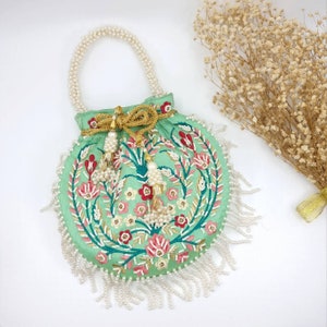 May include: A light green round purse with a floral embroidery design. The purse has a white pearl handle and a white pearl fringe around the bottom.