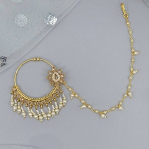 May include: Gold nose ring with a pearl chain and a flower-shaped design with white stones.