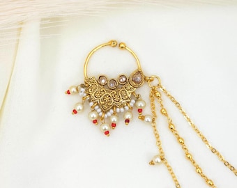 May include: A gold-colored nose ring with a floral design and dangling chains. The ring features faux pearls and red accents, with a central decorative element adorned with small crystals. The design is intricate and ornate, suitable for special occasions.