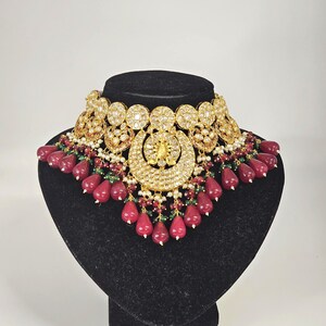 Pu&ograve; includere: Una collana in oro e argento con accenti di pietre preziose rosse e verdi. La collana presenta un grande ciondolo decorato con un motivo floreale. Il ciondolo &egrave; circondato da pietre preziose rotonde pi&ugrave; piccole.