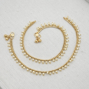 May include: A pair of gold anklets with small white beads. Each anklet has a small bell charm.
